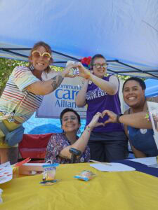 Staff holding hand hearts gathered at yellow table under tent