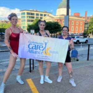 Three CCA staff standing side by side holding colorful banner for Pride Parade in city of Providence.