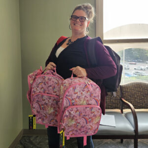 Staff member from FCCP (Family Care Community Partnership) holding backpacks to give to kids.