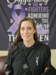 Image of woman wearing a black hoodie and is in front of Recovery Banner with Purple Ribbon and hearts.