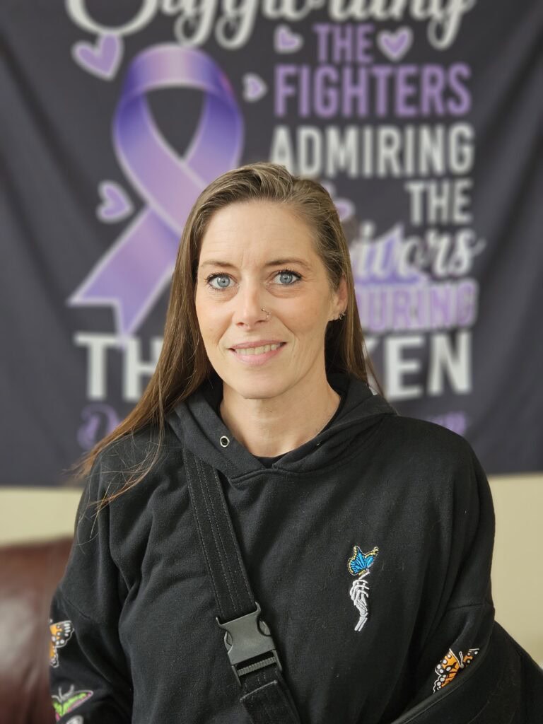 Image of woman wearing a black hoodie and is in front of Recovery Banner with Purple Ribbon and hearts.